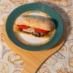 Homemade Italian ground beef sandwich with melted cheddar and gouda cheese, fresh tomatoes, pickles, ketchup, and mustard on toasted Italian bread.